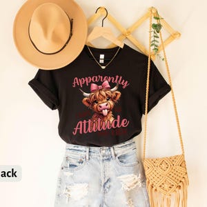 May include: Black t-shirt with a cartoon Highland cow with a pink bow and the text "Apparently I Have An Attitude Problem".