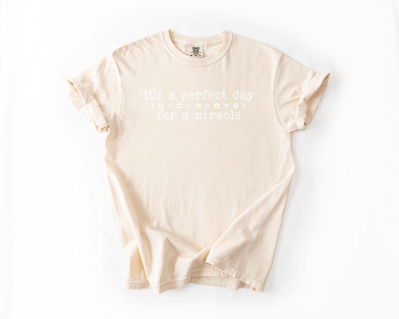 May include: A beige t-shirt with the text "It's a perfect day for a miracle" printed in white.