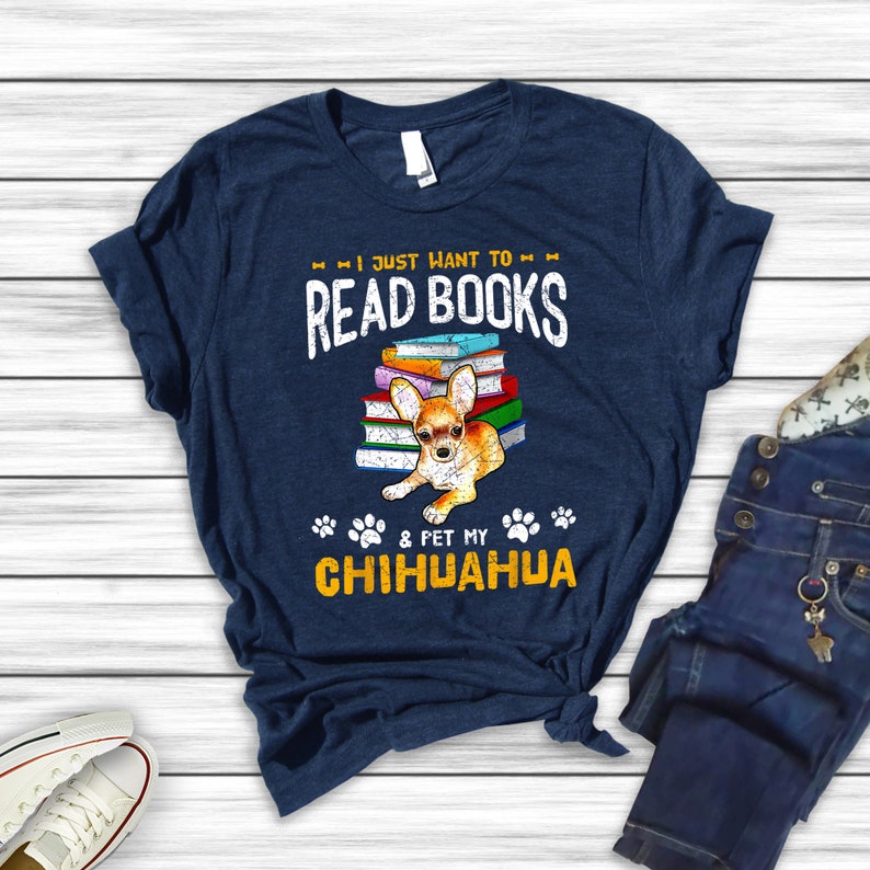 May include: A navy blue t-shirt with the text "I just want to read books & pet my chihuahua" in white and yellow. A chihuahua is sitting on a stack of books.