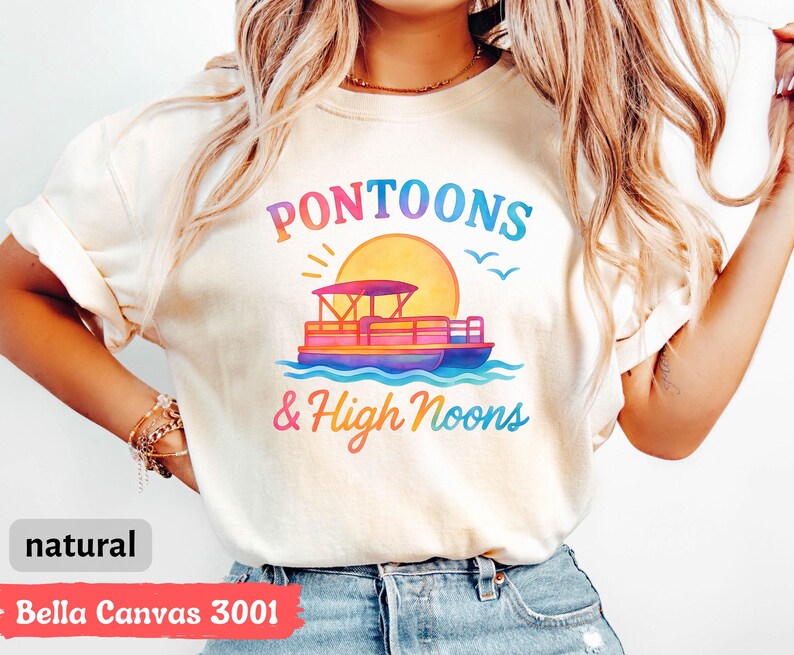 May include: Cream-colored t-shirt with a colorful graphic of a pontoon boat on water, a sun, and the words "Pontoons & High Noons." The shirt is made of Bella Canvas 3001 material.