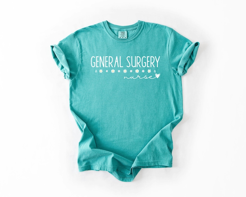 Może przedstawiać: Turkusowa koszulka z napisem "GENERAL SURGERY nurse" w białym kolorze. Tekst jest ozdobiony małymi białymi grafikami kwiat&oacute;w.