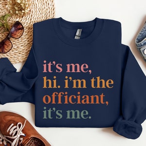 May include: Navy blue sweatshirt with the text "it's me, hi. i'm the officiant, it's me." in colourful lettering.