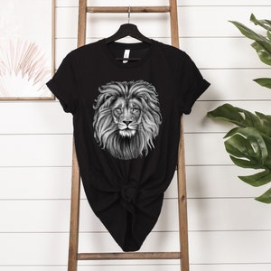 Może przedstawiać: Czarny T-shirt z grafiką przedstawiającą twarz lwa w czerni i bieli.