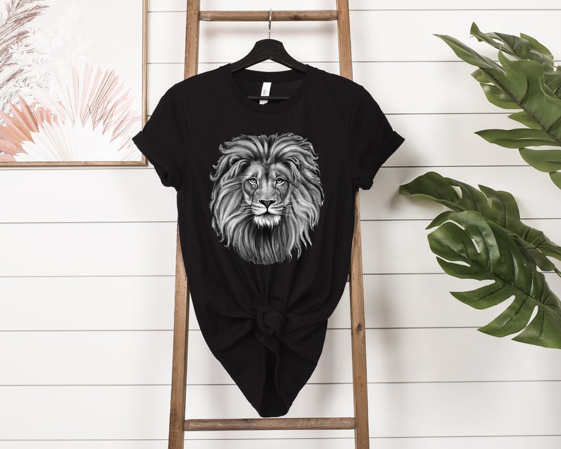 Może przedstawiać: Czarny T-shirt z grafiką przedstawiającą twarz lwa w czerni i bieli.