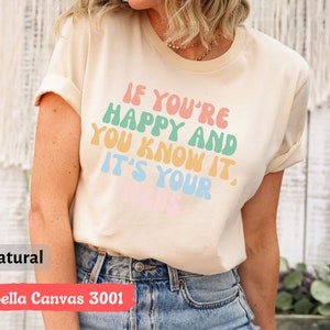 May include: A beige Bella Canvas 3001 t-shirt with the text "If you're happy and you know it, it's your vibe" in rainbow colors.