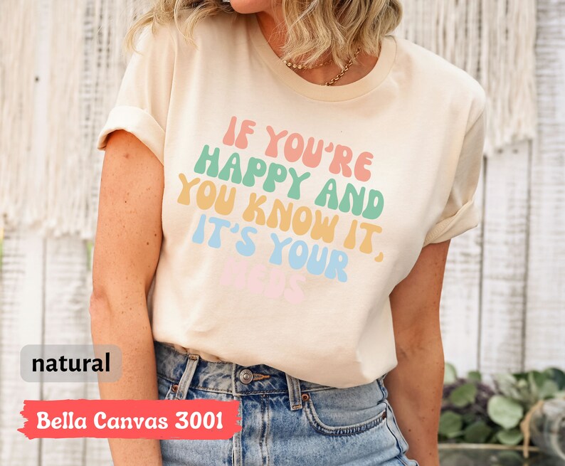 May include: A beige Bella Canvas 3001 t-shirt with the text "If you're happy and you know it, it's your vibe" in rainbow colors.
