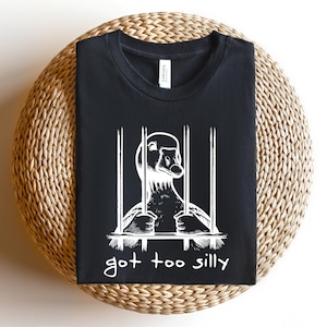 May include: Black t-shirt with a white graphic of a goose in a cage. The text "got too silly" is printed below the image.