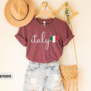 May include: A maroon t-shirt with the word "italy" written in white cursive script and a heart-shaped Italian flag graphic.