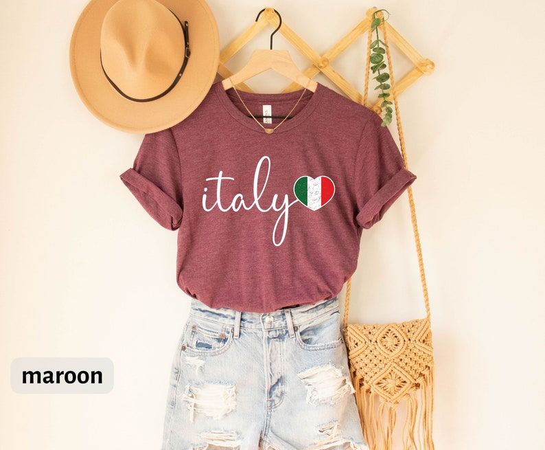 May include: A maroon t-shirt with the word "italy" written in white cursive script and a heart-shaped Italian flag graphic.