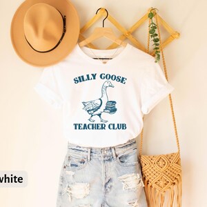 May include: White t-shirt with a blue illustration of a goose carrying books and the text "Silly Goose Teacher Club".