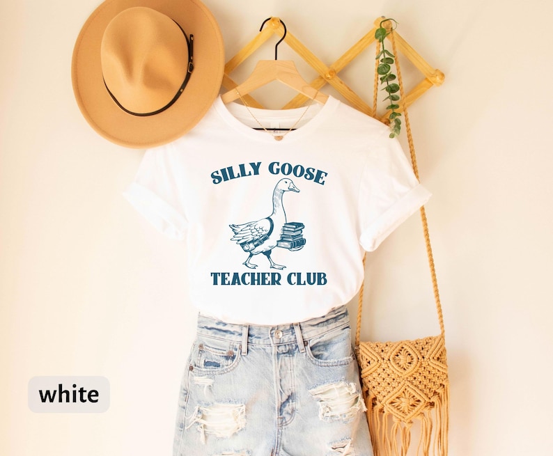 May include: White t-shirt with a blue illustration of a goose carrying books and the text "Silly Goose Teacher Club".