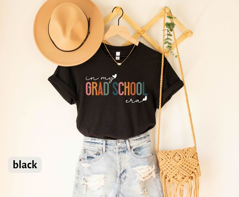 May include: Black t-shirt with the text "in my grad school era" in rainbow colors with a heart and butterfly graphic.