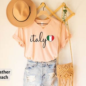 May include: Heather peach colored t-shirt with the text "italy" in black script and a heart with the Italian flag inside.