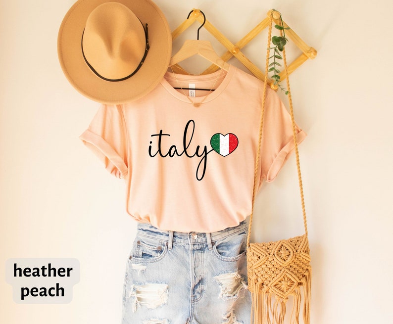 May include: Heather peach colored t-shirt with the text "italy" in black script and a heart with the Italian flag inside.