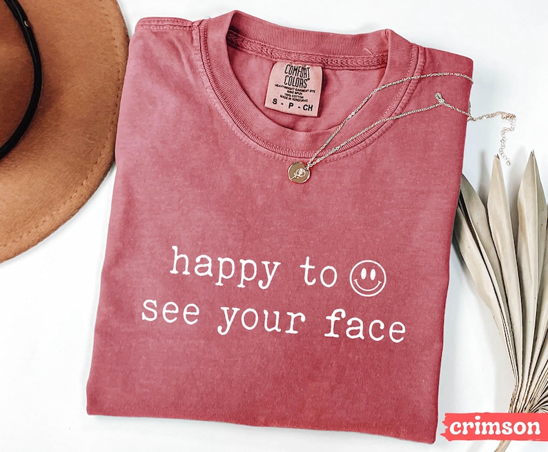 May include: A crimson red t-shirt with the text "happy to see your face" and a white smiley face graphic.