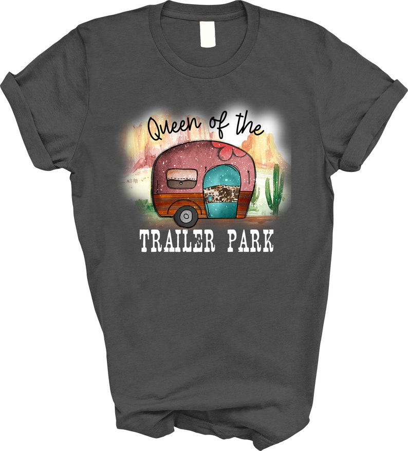 May include: A dark gray t-shirt with the text "Queen of the Trailer Park" in white. The design features a cartoon camper with a pink, turquoise, and brown color scheme.