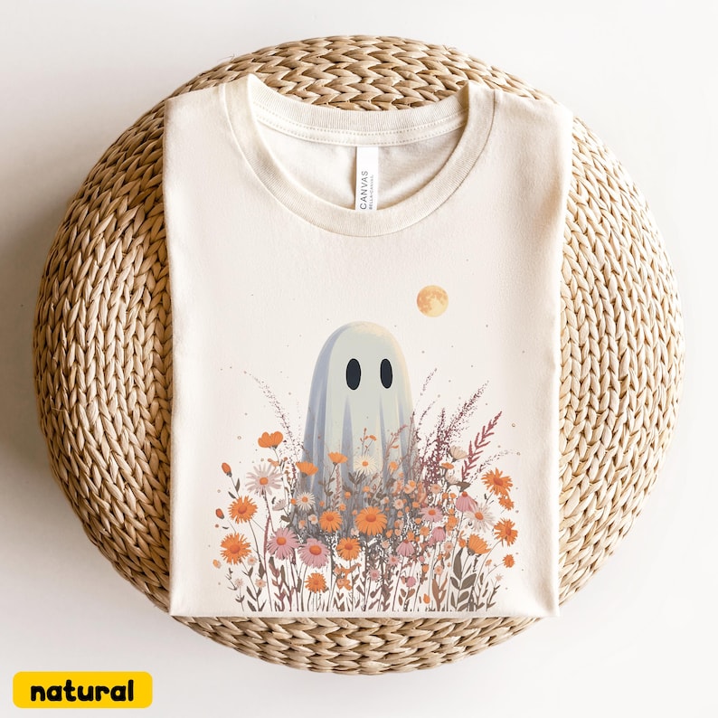 Pu&ograve; includere: T-shirt color crema con un disegno di fantasmino. Il fantasma &egrave; circondato da fiori colorati e una luna piena. La parola "natural" &egrave; stampata in giallo in basso.