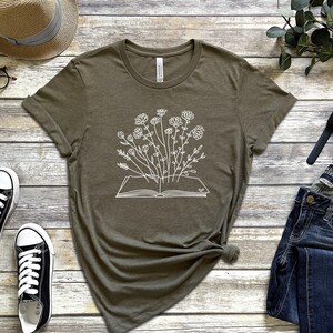 K&ouml;nnte beinhalten: Ein gr&uuml;nes T-Shirt mit einer wei&szlig;en Grafik eines offenen Buches, aus dem Blumen wachsen.