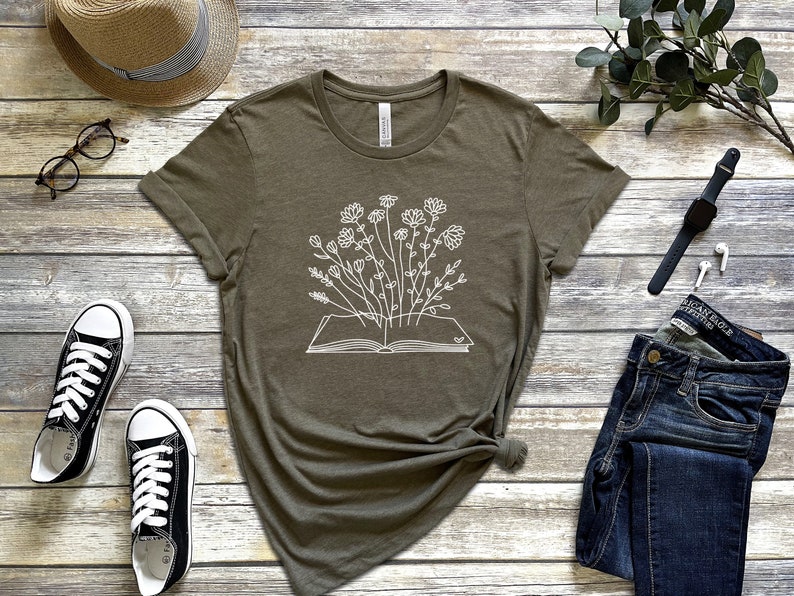 K&ouml;nnte beinhalten: Ein gr&uuml;nes T-Shirt mit einer wei&szlig;en Grafik eines offenen Buches, aus dem Blumen wachsen.