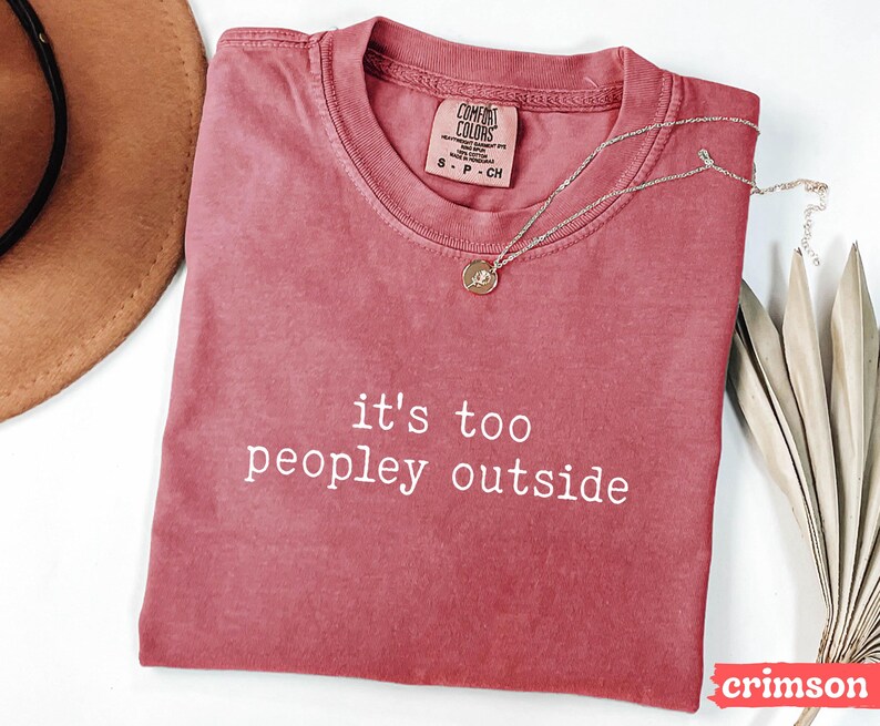 May include: A crimson red t-shirt with the text "it's too peopley outside" printed in white. The shirt is made of a soft, comfortable material.