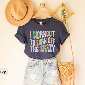 May include: Navy blue t-shirt with the text "I workout to burn off the crazy" in colorful, retro-style lettering.