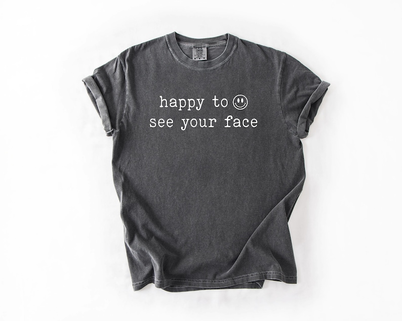 May include: A dark gray t-shirt with the text "happy to see your face" and a smiley face printed in white.