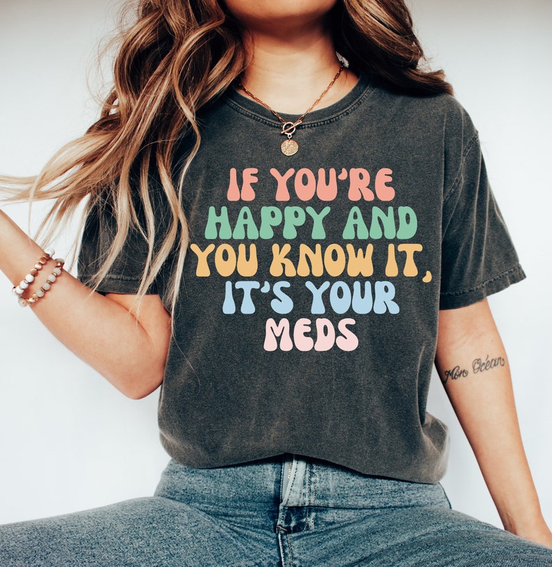 May include: A dark grey t-shirt with the text "If you're happy and you know it, it's your meds" in colorful, rounded letters.