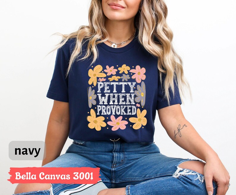 May include: Navy blue t-shirt with the text "Petty When Provoked" in a square design, surrounded by yellow, pink, and gray flowers. The shirt is a Bella Canvas 3001.