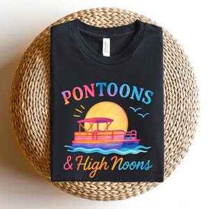 May include: Black t-shirt featuring a colorful graphic of a pontoon boat on water with a sunset and the words "Pontoons & High Noons". The design is in shades of orange, pink, blue, and yellow.
