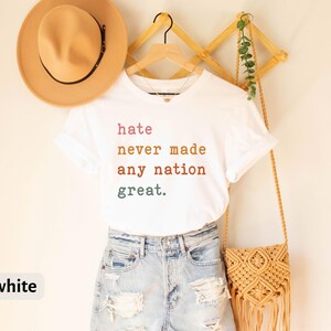 Op de afbeelding: Wit T-shirt met de tekst "hate never made any nation great." in kleurrijke letters.