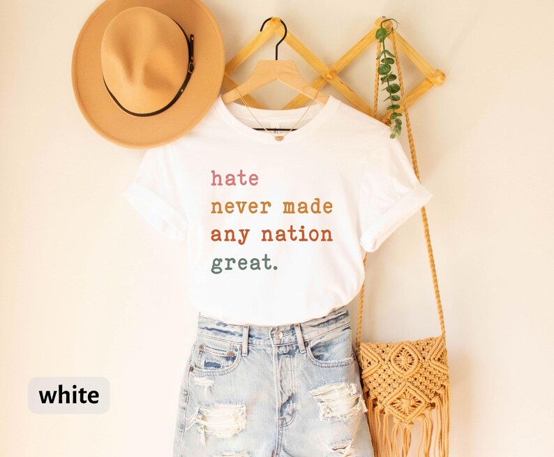Op de afbeelding: Wit T-shirt met de tekst "hate never made any nation great." in kleurrijke letters.