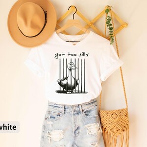 May include: White t-shirt with a black and white illustration of a duck in a cage. The text "got too silly" is written above the duck.