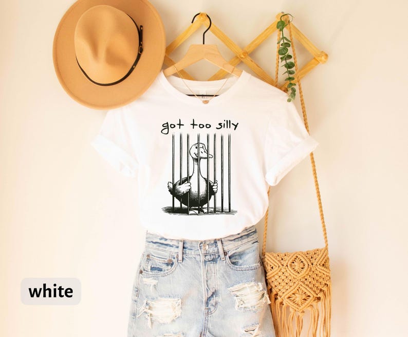 May include: White t-shirt with a black and white illustration of a duck in a cage. The text "got too silly" is written above the duck.