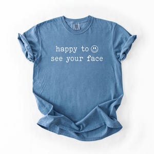 May include: A blue t-shirt with the text "happy to see your face" and a smiley face printed in white.