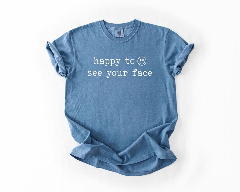 May include: A blue t-shirt with the text "happy to see your face" and a smiley face printed in white.