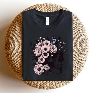 May include: Black t-shirt with a floral skull design. The skull is surrounded by pink flowers and a blue butterfly.