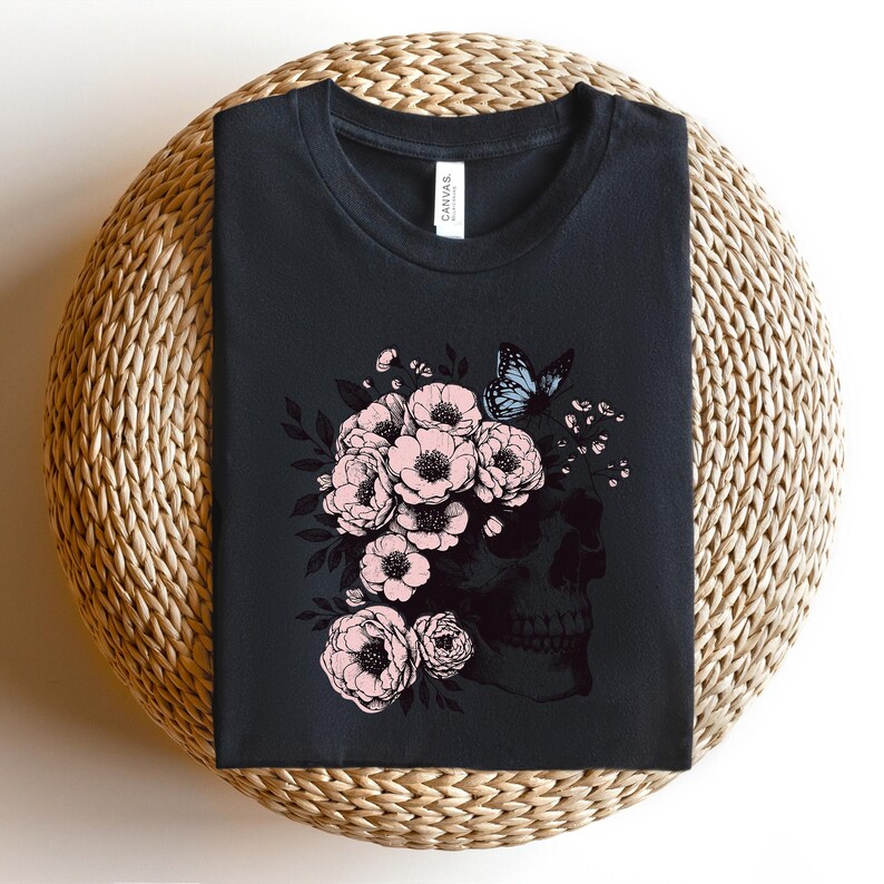 May include: Black t-shirt with a floral skull design. The skull is surrounded by pink flowers and a blue butterfly.