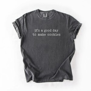 May include: A dark grey t-shirt with the text "it's a good day to make cookies" printed in white.