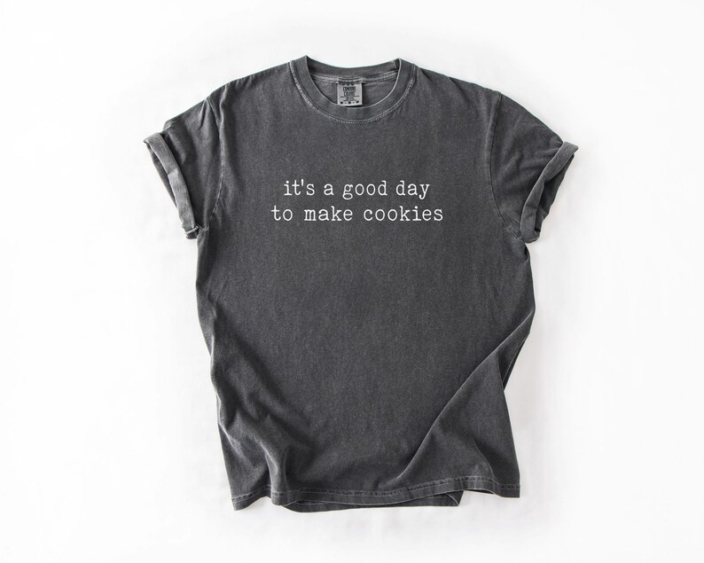 May include: A dark grey t-shirt with the text "it's a good day to make cookies" printed in white.