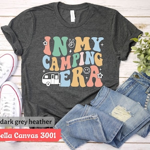 May include: A dark grey heather Bella Canvas 3001 t-shirt with the text "In My Camping Era" in colorful retro letters. A small camper van graphic is below the text.