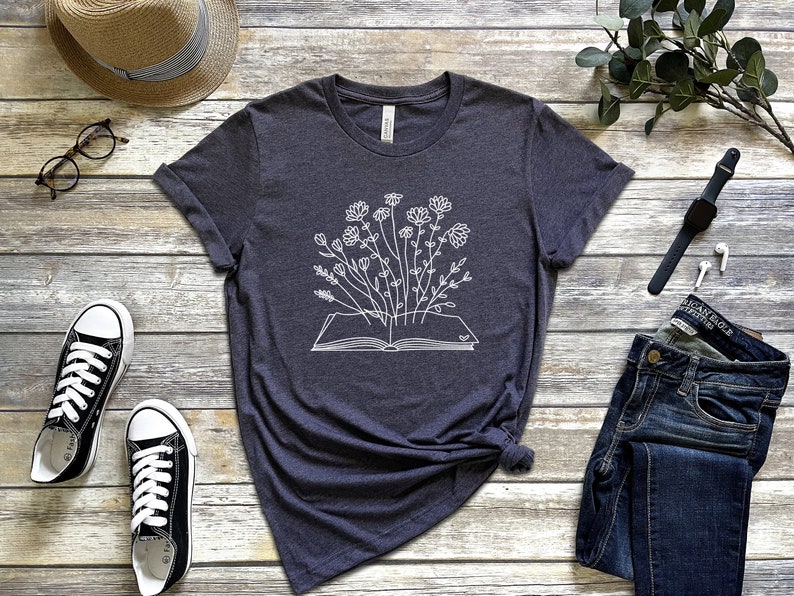 K&ouml;nnte beinhalten: Ein dunkelgraues T-Shirt mit einem wei&szlig;en Umriss eines Buches, aus dem Blumen wachsen.
