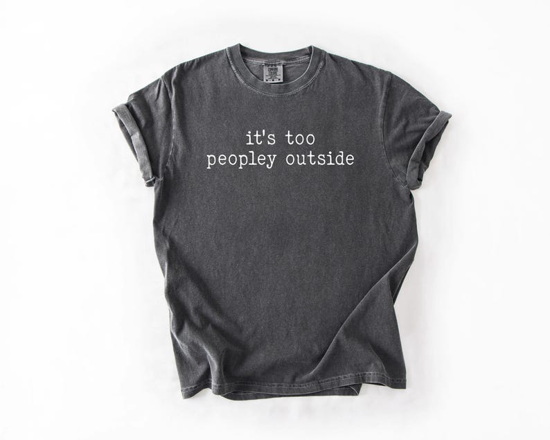 May include: A dark gray t-shirt with the text "it's too peopley outside" printed in white.