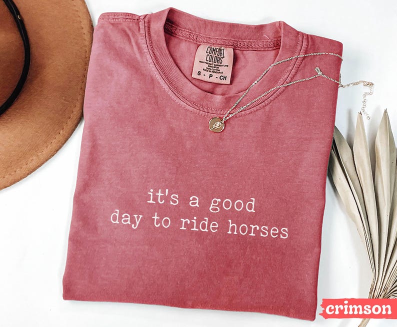 May include: A crimson red t-shirt with the text "it's a good day to ride horses" in white. The shirt is made of a soft, comfortable material and has a relaxed fit.