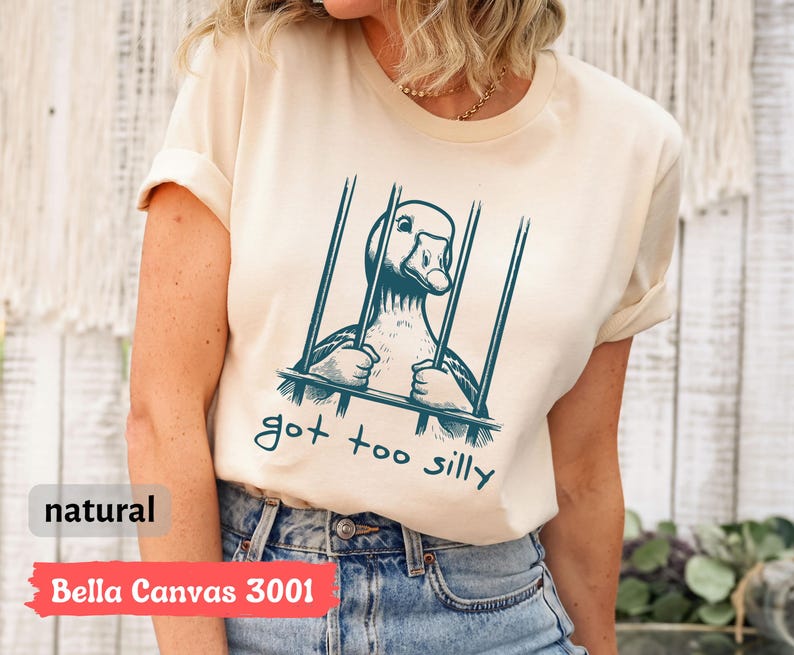 May include: A beige t-shirt with a graphic of a goose in a cage and the text "got too silly".