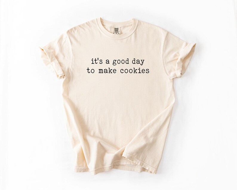 May include: A beige t-shirt with the text "it's a good day to make cookies" printed in black.
