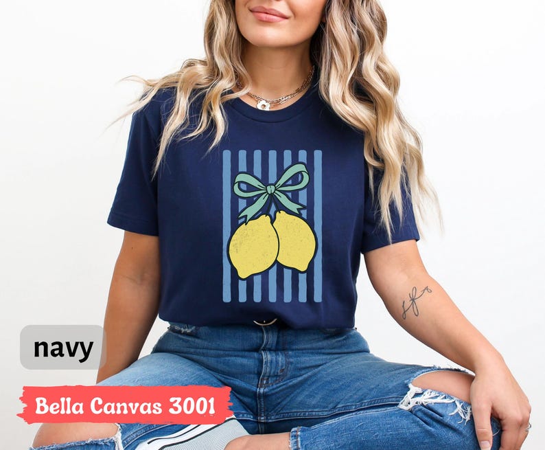 May include: A navy blue t-shirt with a graphic of two lemons tied together with a blue bow on a blue and white striped background. The text "Bella Canvas 3001" is printed on the bottom of the shirt.