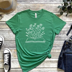 K&ouml;nnte beinhalten: Ein gr&uuml;nes T-Shirt mit einer wei&szlig;en Grafik eines offenen Buches, aus dem Blumen wachsen.