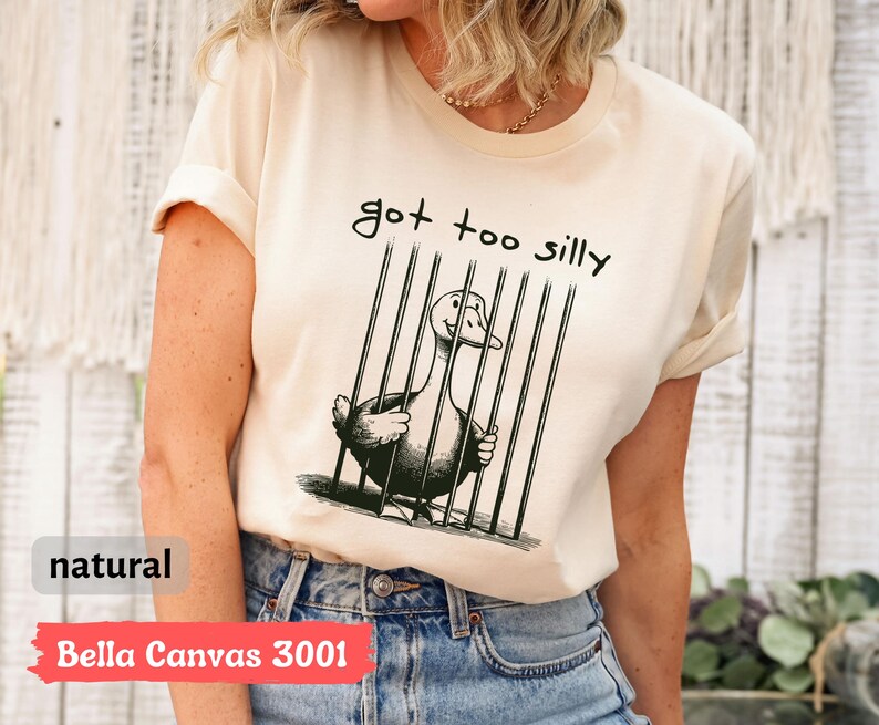 May include: A white t-shirt with a black and white illustration of a goose in a cage. The text "got too silly" is printed on the shirt.