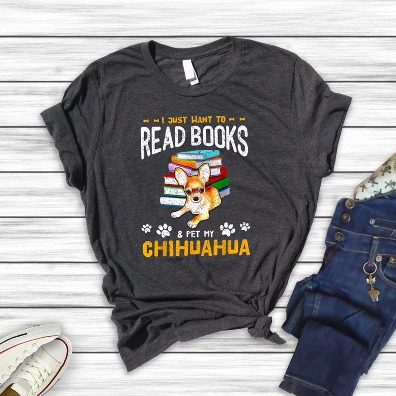 May include: A dark gray t-shirt with the text "I just want to read books & pet my chihuahua" in yellow and white. A chihuahua is sitting on a stack of books.