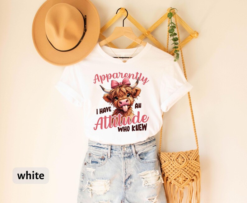 May include: White t-shirt with a cartoon Highland cow wearing a pink bow and the text "Apparently I have an attitude who knew".
